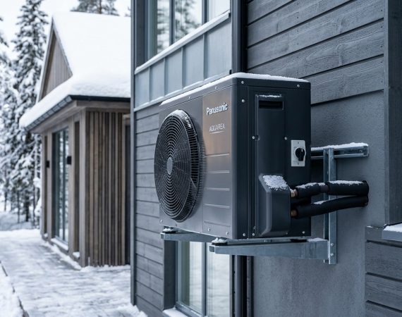 Modern cold-climate heat pump outdoor compressor operating during sub-zero winter snow on contemporary residential exterior